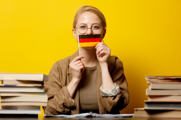 Stil blonde Frau sitzt am Tisch mit Büchern und Flagge von Deutschland auf gelb