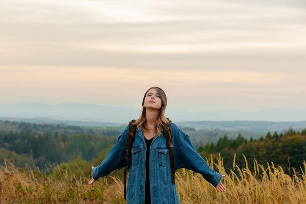 Stil Frau in Jeansjacke und Hut mit Rucksack in der Landschaft mit Bergen