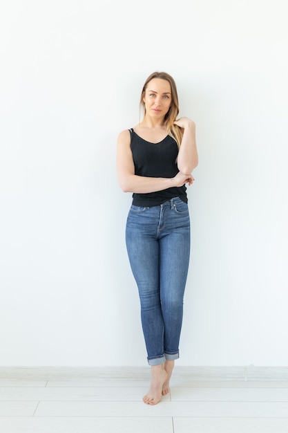 Stil- und Personenkonzept - junge Frau in Jeans, die über der weißen Wand steht und wie sexy aussieht