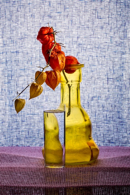 Foto stilleben mit einer gelben vase, einem glas wasser und einem zweig physalis