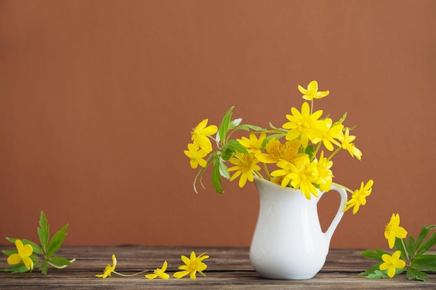 Stilleben mit gelben Frühlingsblumen im Krug auf braunem Hintergrund