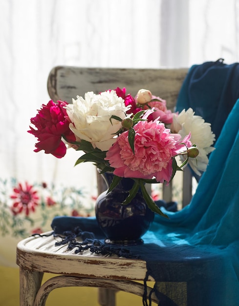 Stilleben mit weißen und rosa Pfingstrosen in einer blauen Vase auf einem Vintaje-Stuhl