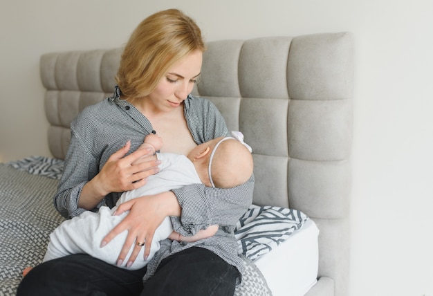 Stillkonzept. Schöne junge Frau, die ihr Kleinkindbaby auf der Couch zu Hause stillt, Kopienraum