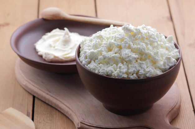 Stillleben auf einem hölzernen Hintergrund Quarkmasse und Hüttenkäse auf einem Tonteller auf einem Holzbrett Nahaufnahme gesunder Frühstücksspeisen