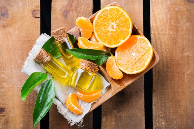 Stillleben-Konzept für Gesundheit und Schönheit Organisches ätherisches Mandarinen-Mandarinen-Clementinenöl in einem kleinen Glasgefäß mit grünen Blättern und Orangenfrüchten auf einem rustikalen Holztisch Draufsicht