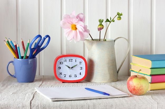 Stillleben mit Album, Wecker, Apple und Lehrbüchern.