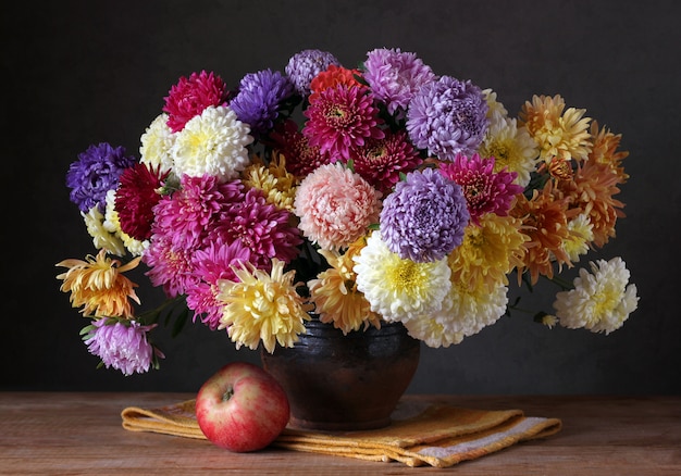 Stillleben mit einem Blumenstrauß von Chrysanthemen in einem Krug und in einem roten Apfel.