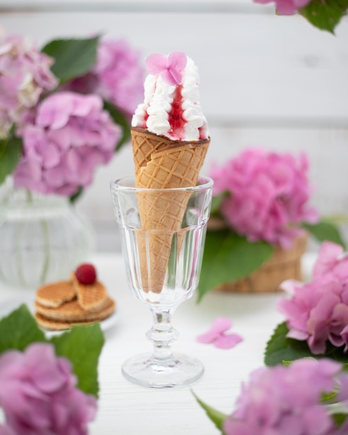 Stillleben mit einer Eistüte im Glas und Blumen daneben