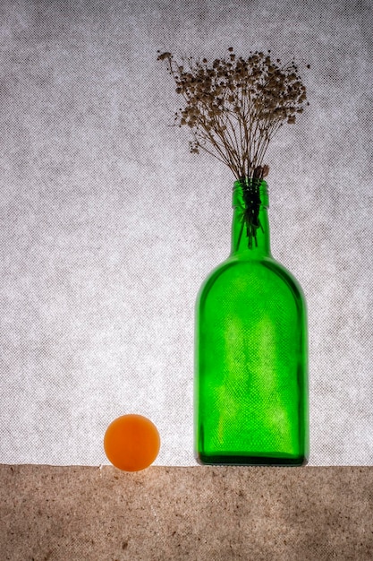Stillleben mit einer grünen Flasche mit Blumen und einer orangefarbenen Kugel