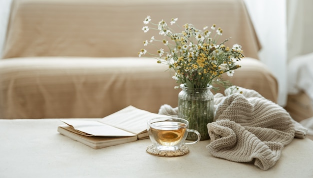 Stillleben mit einer Tasse Kräutertee, einem Strauß Wildblumen, einem Buch und einem Strickelement.