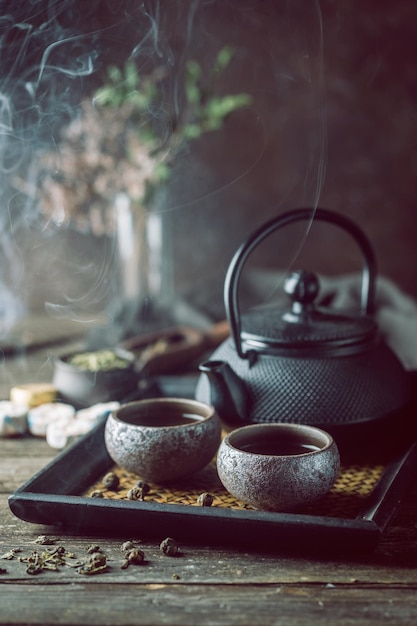 Stillleben mit japanischem gesundem grünem Tee in kleinen Tassen und Teekanne auf dunklem Hintergrund