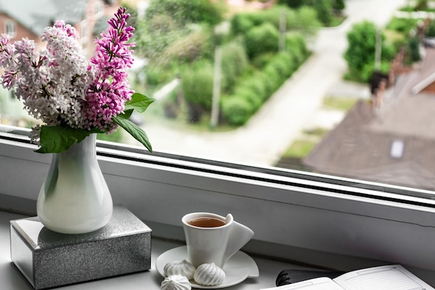 Stillleben mit lila Blumen in einer weißen Vase auf der Fensterbank Notizblock für Notizen und eine Tasse Kaffee gemütliches Zuhause Geschäftsplanung