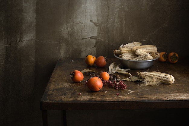 Stillleben mit Obst und Mais in einer Aluminiumschale auf einem alten Holztisch