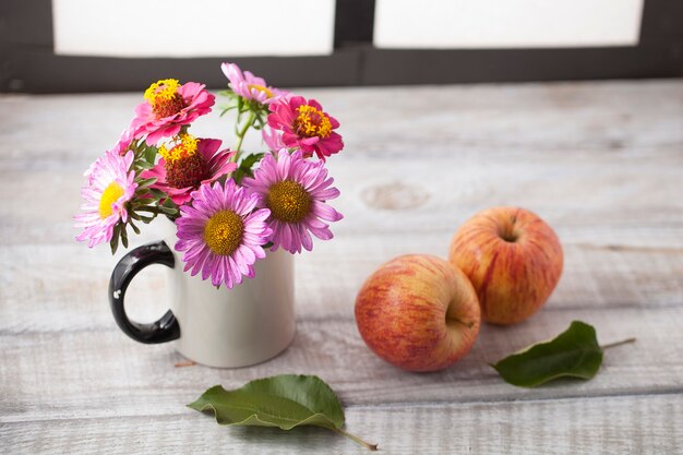 Stillleben mit Äpfeln und Blumen auf einer Holzfläche am Fenster