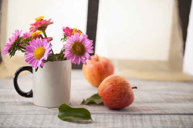 Stillleben mit Äpfeln und Blumen auf einer Holzfläche am Fenster