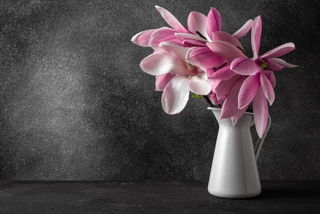 Stillleben mit rosa Magnolienblumenstrauß in Vase auf schwarzer Oberfläche