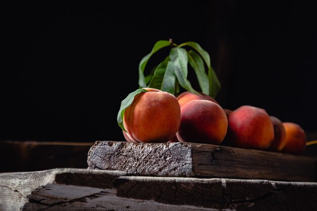 Stillleben Pfirsiche auf Holztisch Schneidebrett Messer Dunkle Stimmung. Saftige reife Pfirsiche auf dunklem rustikalem Holztisch. Köstliche Bauernpfirsiche mit Blättern ganze Frucht in Hälften, Pfirsich mit Knochen.