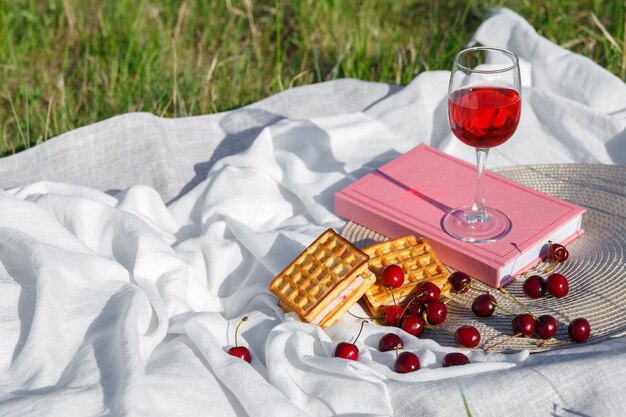 Stillleben und Essensfoto Kirsch- und Waffelbeeren liegen auf runder Korbserviette und wellenförmigem Stoff Glas Kirschsaft oder Wein