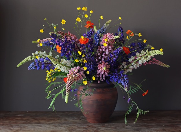 Stilllebenblumenstrauß mit Lupine und Butterblumeen in einem Lehmkrug auf Dunkelheit