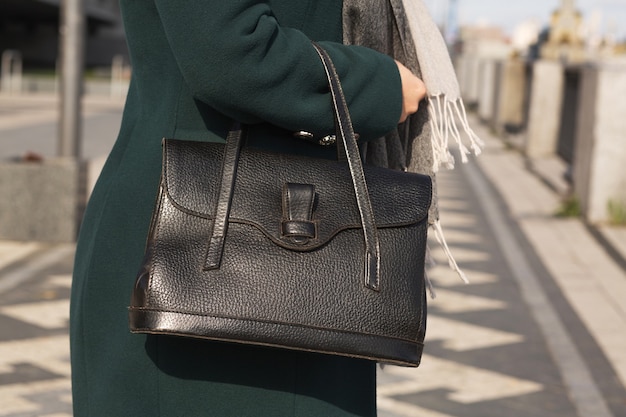 Stilvoll gekleidete Frau im grünen Mantel mit schwarzer Ledertasche. Nahaufnahme