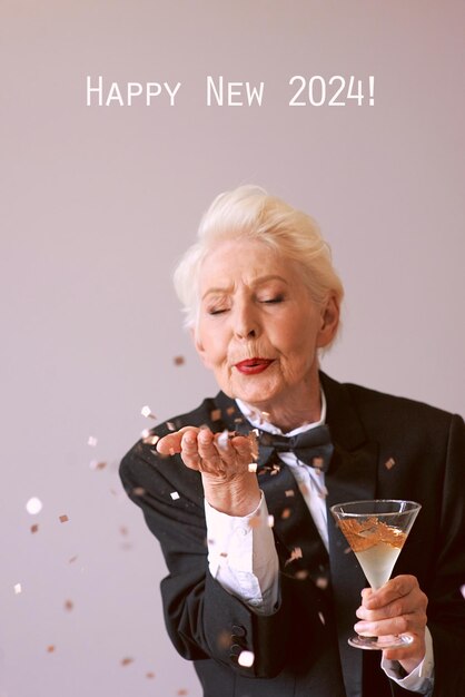 Stilvolle ältere Frau im Smoking mit einem Glas Champagner, das Konfetti bläst und das neue Jahr feiert