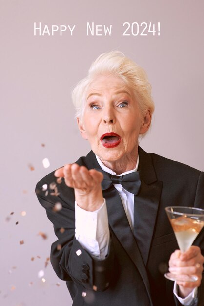 Stilvolle ältere Frau im Smoking mit einem Glas Champagner, das Konfetti bläst und das neue Jahr feiert