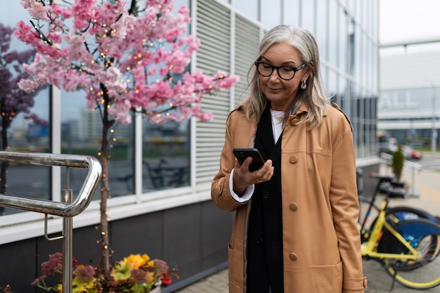 Stilvolle ältere Frau mit Handy in der Hand in der Stadt