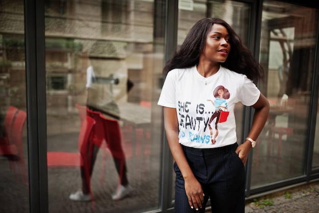 Foto stilvolle afrikanisch-amerikanische frau in bedrucktem t-shirt posierte im freien gegen fenster