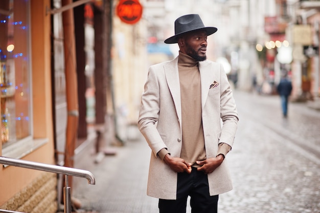Stilvolle Afroamerikaner tragen beige Jacke und schwarze Hutpose an der Straße.