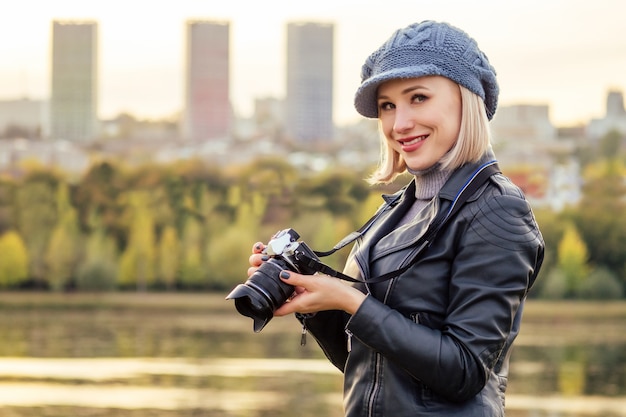 Stilvolle blonde Frau in blauem französischem Barettfotograf fotografiert den Herbstwald bei Sonnenuntergang