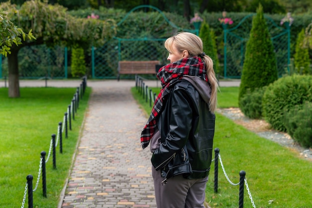 Stilvolle blonde Frau in schwarzer Lederjacke, die im Park eine schöne modische Frau spaziert