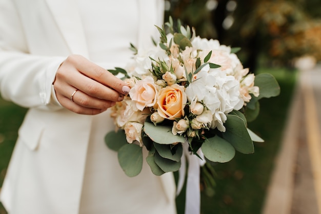 Stilvolle Braut in einem weißen Kleid und Maniküre mit einem Hochzeitsstrauß