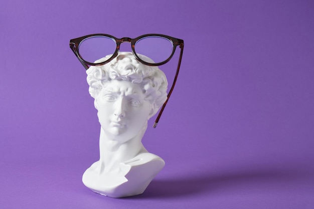 Stilvolle Brillen mit Gipsskulptur auf violettem, trendigem Farbhintergrund, Kopierraum David-Büste