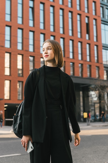Stilvolle Dame in dunkler Kleidung steht gegen moderne Architektur