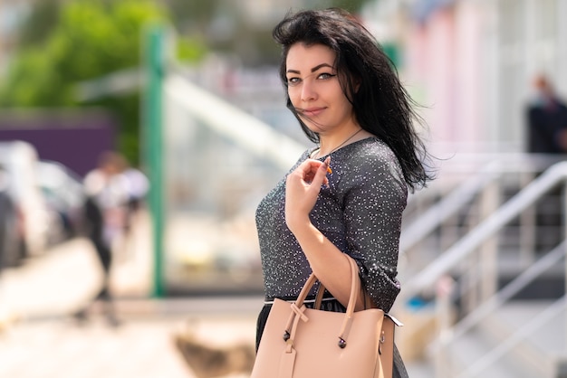 Stilvolle dunkelhaarige Frau, die draußen in der Stadt mit einer Lederhandtasche geht