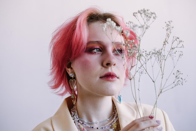 Stilvolle Frau der jungen Mode, die mit hellem Make-up des Gypsophila-Zweigs und gefärbtem Haar aufwirft