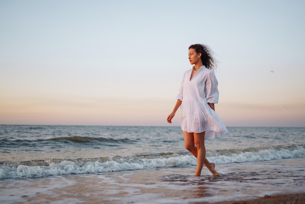 Stilvolle Frau im eleganten weißen Kleid posiert am Meer Sommerzeit Reisewochenende entspannen