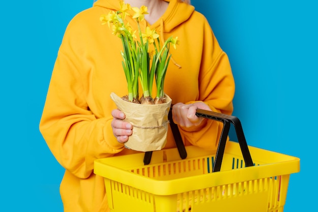 Stilvolle Frau im gelben Hoodie mit gelbem Korb und Blumen auf blauem Hintergrund