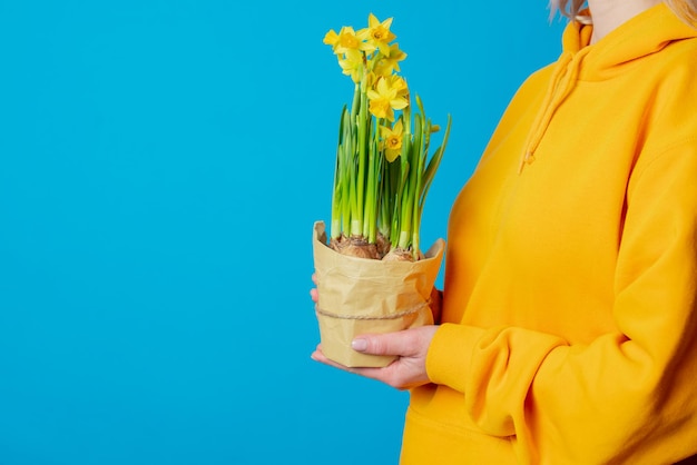 Stilvolle Frau im gelben Hoodie mit Narzissenblumen auf blauem Hintergrund