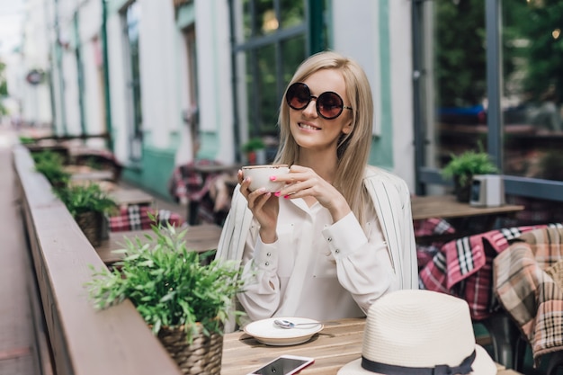 Stilvolle Frau in der Sonnenbrille, die in einem Sommercafé sitzt