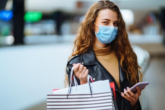 Stilvolle Frau in medizinischer Schutzmaske mit Einkaufstasche mit ihrem Telefon Modestil Blackfriday