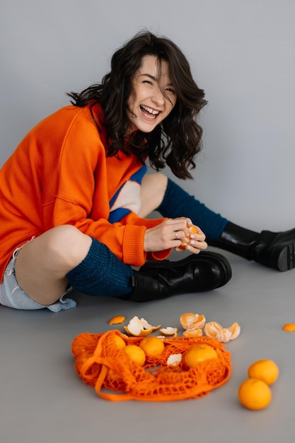 Stilvolle Frau in orangefarbener Strickjacke, die für ein Foto in einem Fotostudio auf grauem Papierhintergrund posiert Helle Emotionen stellen ein modernes Konzept dar