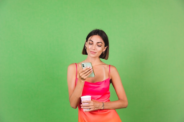 Stilvolle Frau in rosa Seidenkleid einzeln auf Grün glücklich mit einem Lächeln auf dem Handybildschirm, Nachrichtennachrichten lesen read
