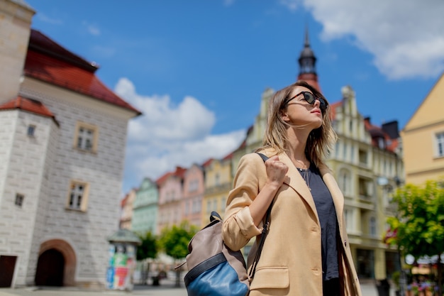 Stilvolle Frau in Sonnenbrille und Rucksack im gealterten Stadtzentrumplatz