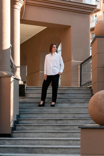 Stilvolle Geschäftsfrau auf der Treppe des Gebäudes Erfolgreiche Frau ist in Hemd und Hose im klassischen Stil gekleidet