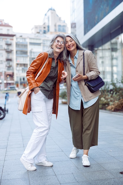 Stilvolle glückliche ältere Frauen stehen am Herbsttag auf der modernen Stadtstraße