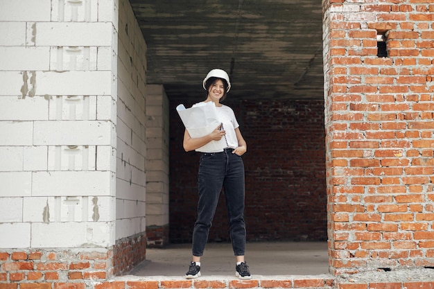 Stilvolle, glückliche Architektin, die Baupläne im Hausbau auf der Baustelle überprüft Junge Ingenieurin oder Bauarbeiterin in Hardhat mit Plänen für ein neues modernes Haus