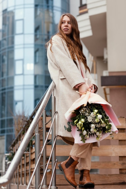 Foto stilvolle glückliche frau, die blumenstrauß draußen hält