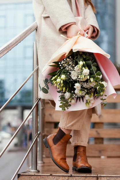 Stilvolle glückliche Frau, die Blumenstrauß draußen hält