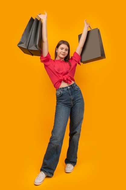 Stilvolle glückliche junge Frau hält mehrere Papiertüten nach dem Einkauf Gelber Hintergrund Black Friday Concept Vertikaler Rahmen